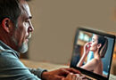 a sad-looking man gazing at a laptop screen that bears the image of his beloved AI woman