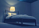 a bed in a darkened room with a single lamp on