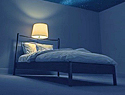 a bed in a darkened room with a single lamp on