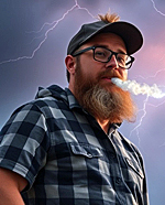 A bearded man in a flannel shirt and trucker's cap exhaling a huge cloud of smoke.