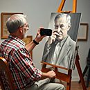 A baby curiously touching a man's face while he lies on grass.