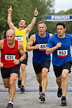 Finish line mistakes as a runner celebrates too early with arms raised while three runners sprint past him toward the finish line in a road race.