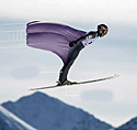 Ski jumper in mid-flight demonstrating strategic genital enhancement aerodynamic advantage, with technical annotations indicating enhanced surface area in jumpsuit and airflow patterns