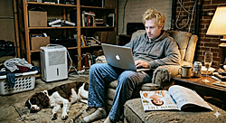 Accidental wedding planner consults laptop in cluttered basement while dog sleeps at his feet and a bridal magazine lies open on the ottoman. Priorities.