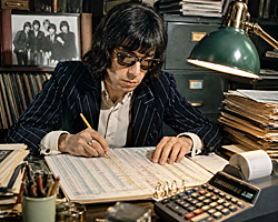 Bill Wyman carefully updating a sprawling spreadsheet at a cluttered desk, imagining Bill Wyman as rock's most meticulous record keeper.