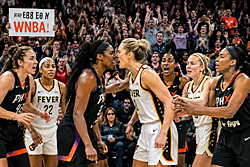 WNBA fights erupt on the court as two players confront each other, teammates gather around, and excited fans cheer from the crowded stands.